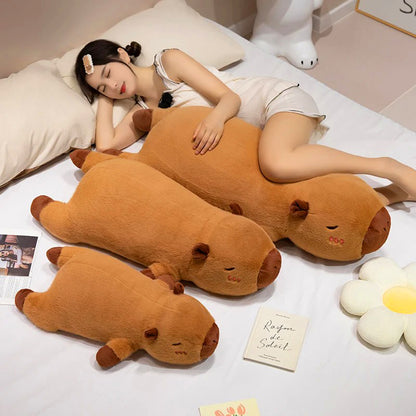 Woman snuggling in bed with three different-sized capybara plush toys, showing soft material and size options.