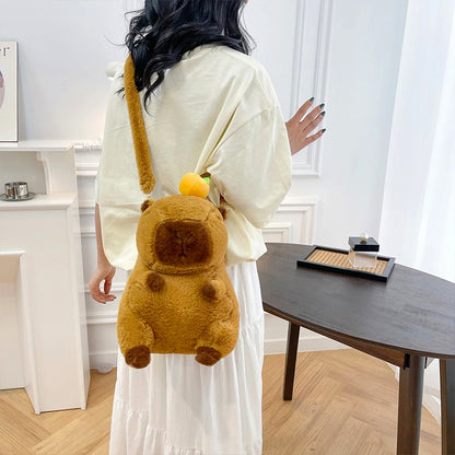 Girl wearing fuzzy capybara backpack with orange fruit detail, seen from the back in a softly lit indoor room.