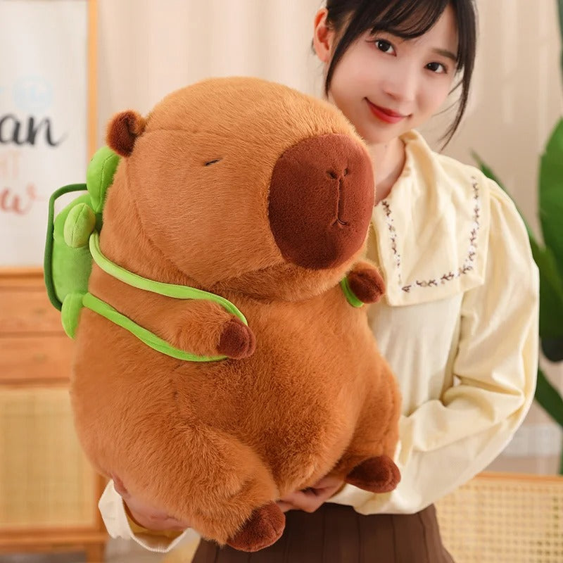 Smiling girl holding a large capybara plush with green turtle backpack – soft and cuddly stuffed animal gift for kids or plush lovers.