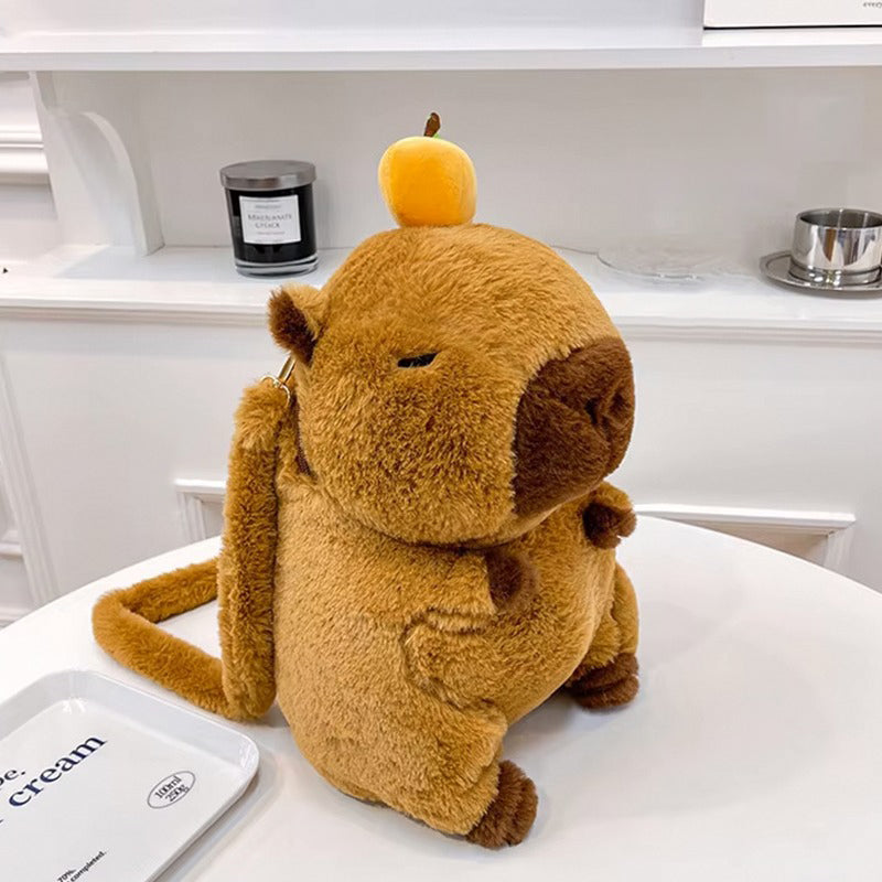 Plush capybara backpack with sleepy expression and cute orange hat, sitting upright on white tabletop.