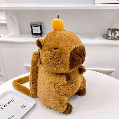 Plush capybara backpack with sleepy expression and cute orange hat, sitting upright on white tabletop.