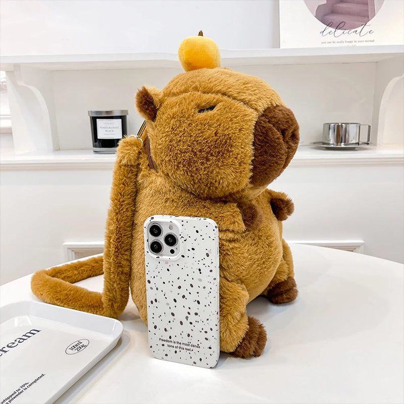 Cute capybara plush backpack shown beside phone for size reference on white table