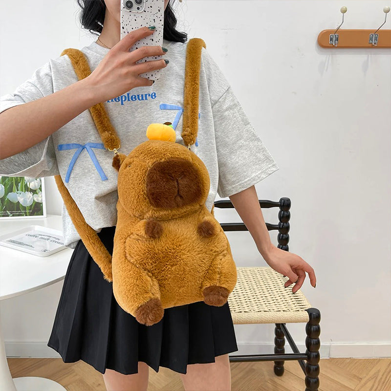 Girl taking mirror selfie wearing capybara plush backpack with yellow fruit hat