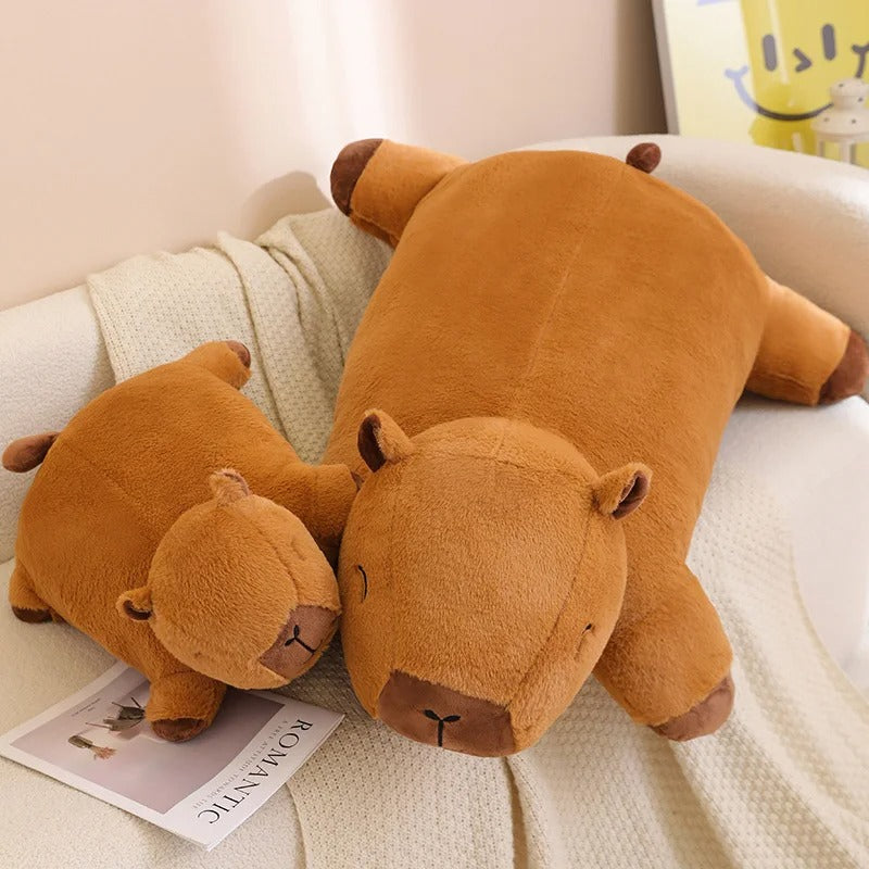 Large and small capybara plush pillows displayed together on a couch, soft stuffed animals for cuddles.
