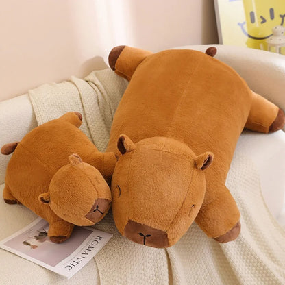 Large and small capybara plush pillows displayed together on a couch, soft stuffed animals for cuddles.