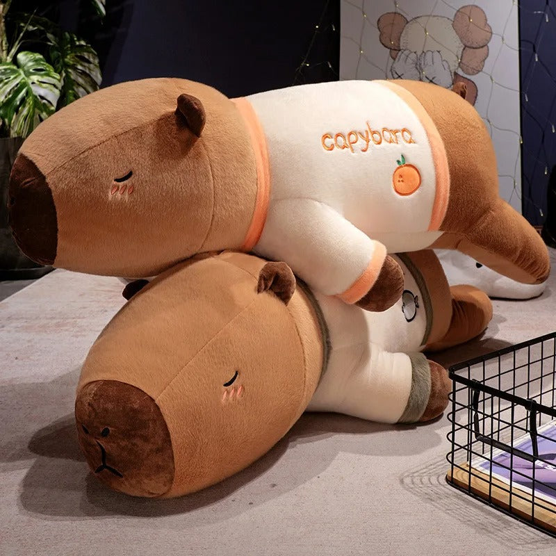 Two giant capybara plush stuffed animals wearing pajamas stacked together on the floor.