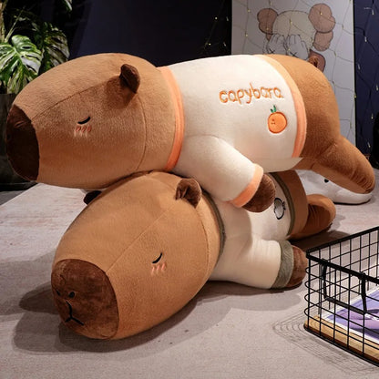 Two giant capybara plush stuffed animals wearing pajamas stacked together on the floor.