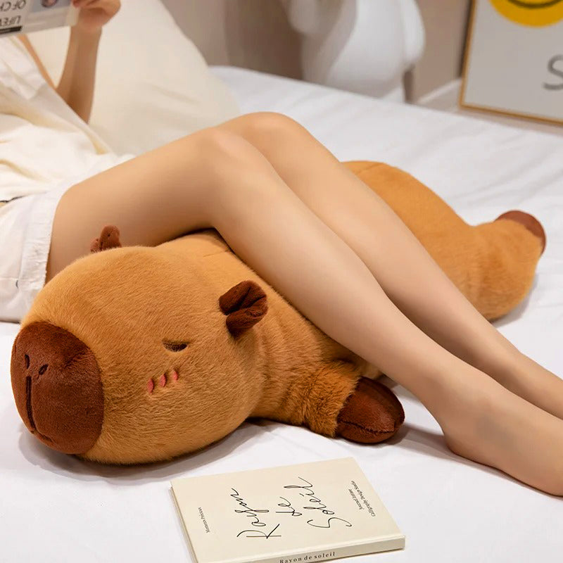Girl lounging with large capybara plush toy used as a leg pillow for cozy and supportive relaxation.