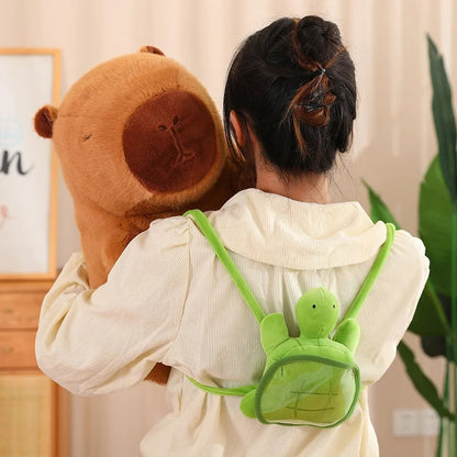 Girl seen from behind wearing a turtle-shaped mini backpack while hugging a large capybara plush toy that has a matching turtle backpack, creating a coordinated and adorable look.