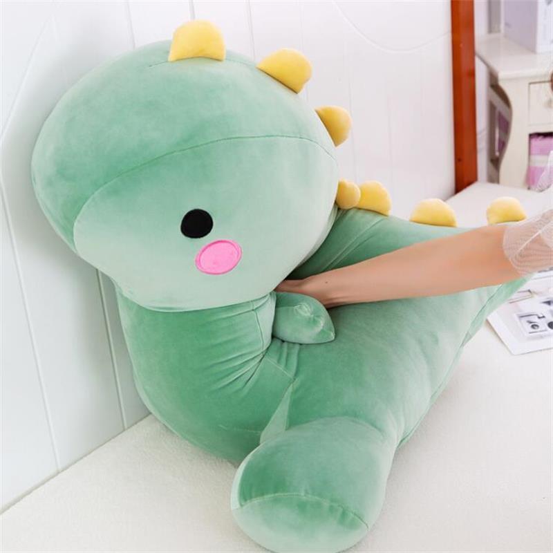 Kawaii collection giant green dinosaur plushie being squeezed to show its soft and squishable marshmallow texture. This high-quality dino stuffed animal features a plush round head, pink cheeks, and yellow spikes, designed for ultimate comfort and cute room aesthetic.
