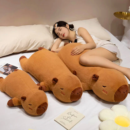 Woman sleeping next to trio of capybara plush toys in small, medium, and large sizes for cuddling.